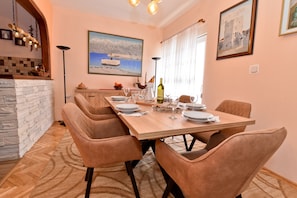 A dining room with a wooden table set for six, a stone fireplace, and a large painting of a coastal scene.