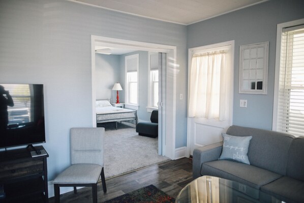 A living room with a television, a sofa, a chair, and a bed in the adjacent room.
