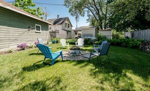 Un jardin avec un foyer, des fauteuils Adirondack verts et blancs, et une pelouse bien entretenue.