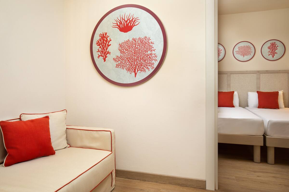 A hotel room with a sofa and two beds, each with red and white bedding.