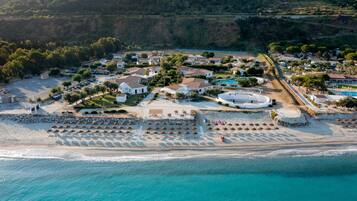 Eine Luftaufnahme eines Küstenresorts mit Strand, Villen und einem Poolbereich.