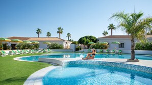 A pool area with a person sitting on the edge, surrounded by lounge chairs and umbrellas. - VOI Le Muse Essentia (Zambrone)