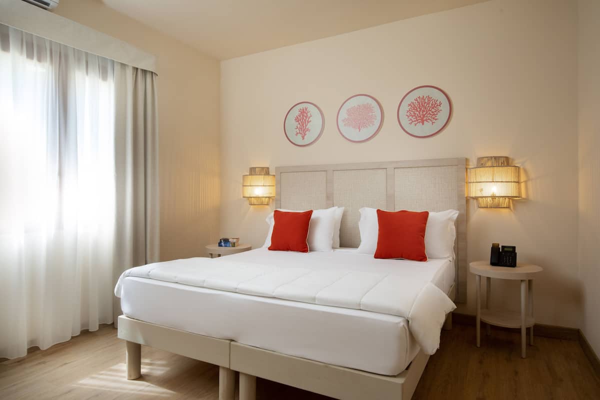 A hotel room with a large bed, two bedside tables, a lamp, and three wall art pieces.