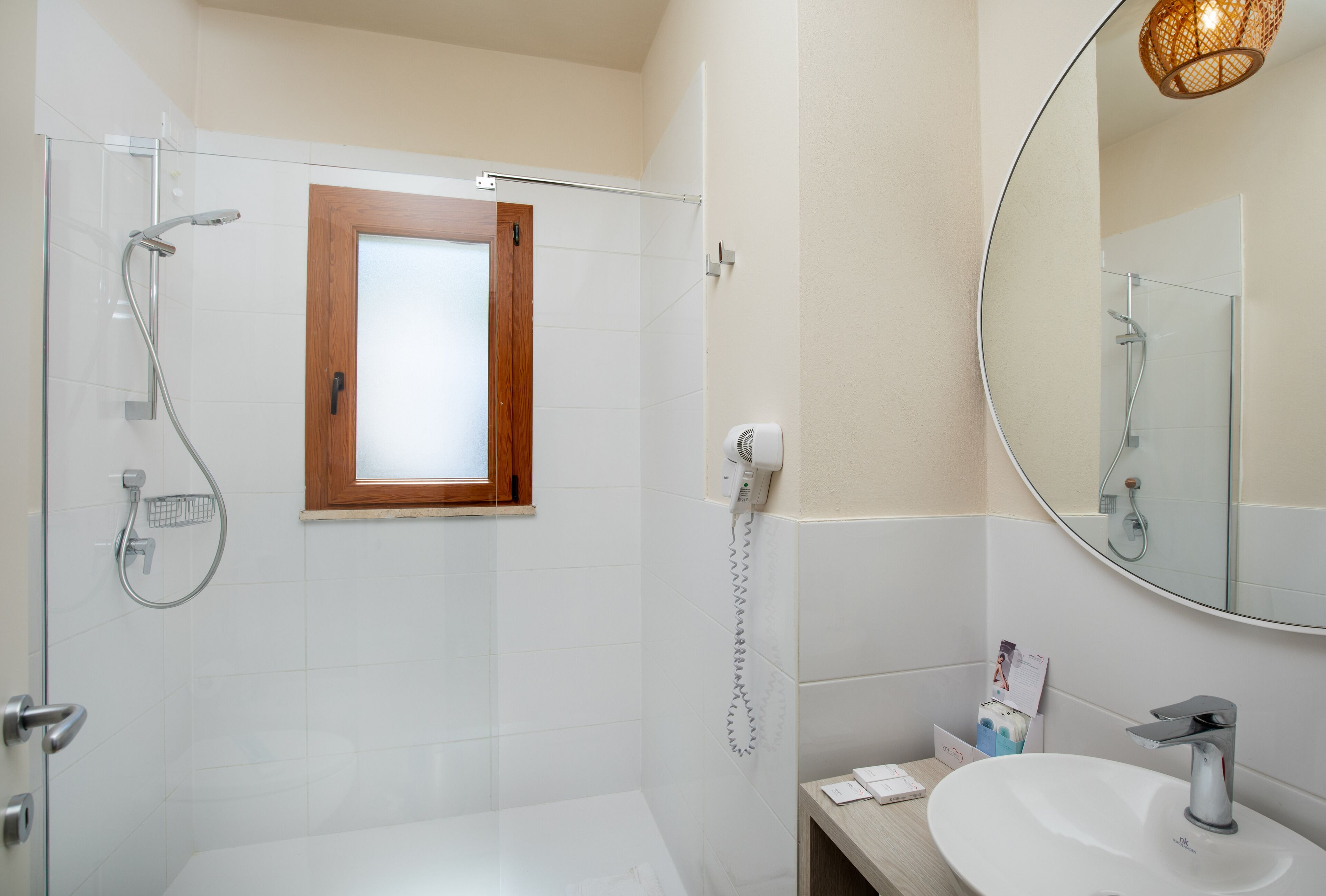 Un bagno moderno con cabina doccia in vetro, finestra con cornice in legno, asciugacapelli e un grande specchio.
