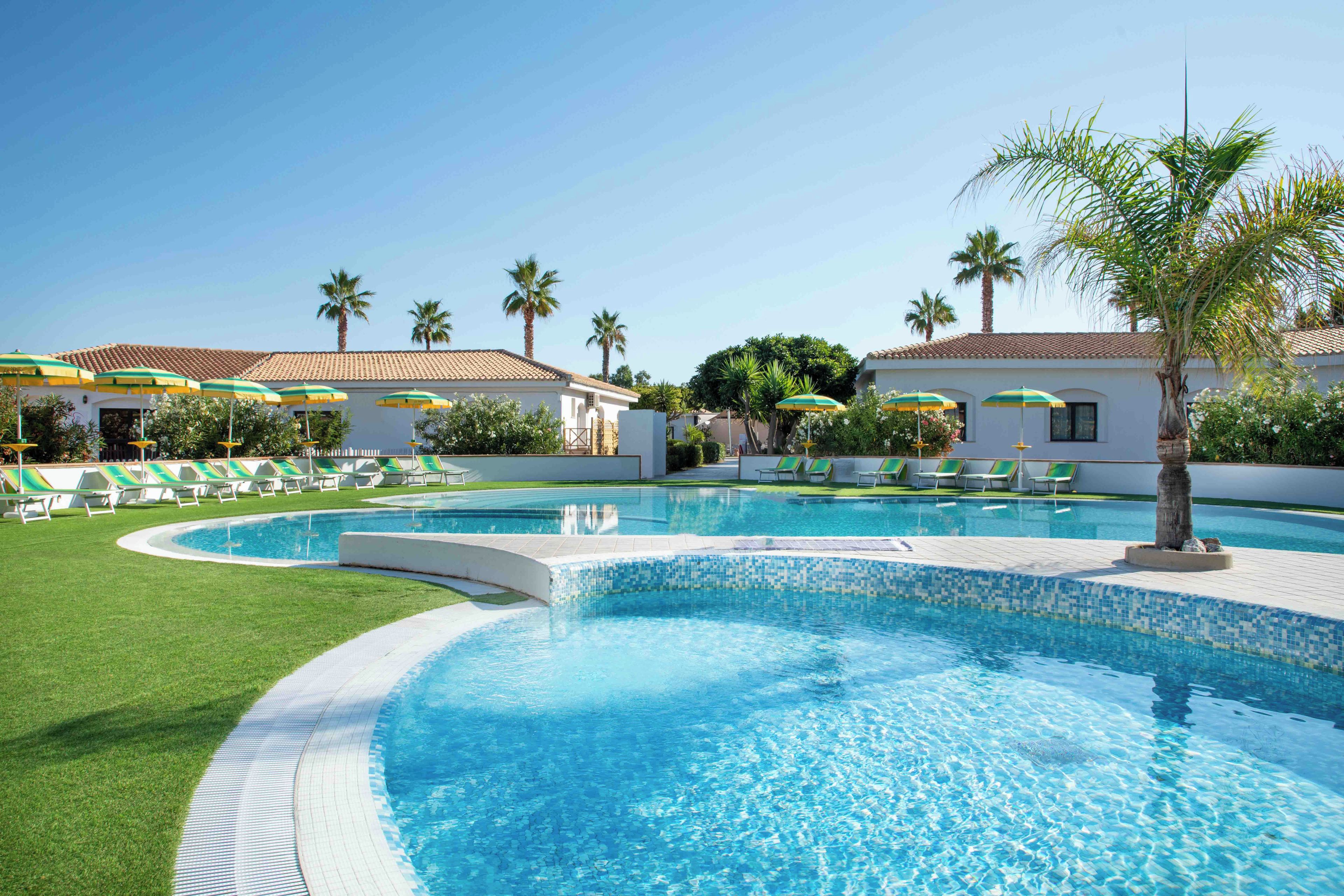 Una piscina con bordo piastrellato, circondata da erba verde e palme.