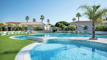 Una piscina con bordo piastrellato, circondata da erba verde e palme.
