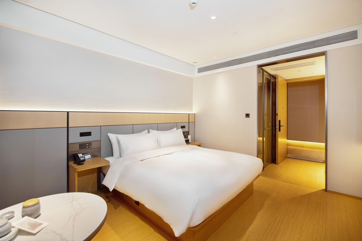 A hotel room with a neatly made bed, a bedside table with a phone and a lamp, and a small round table with a white tablecloth.