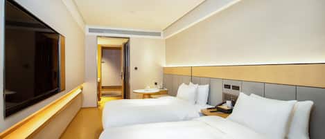A hotel room with two beds, a TV, a bedside table, and a small round table with a lamp.