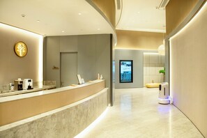 A modern reception area with a marble counter, a digital information screen, and a seating area with a massage chair. - Ji Hotel (Chongqing)