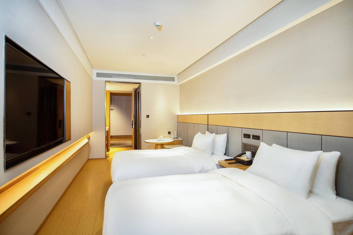 A hotel room with two beds, a TV, a bedside table, a small round table, and a door leading to another room.