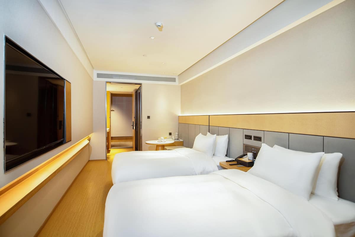 A hotel room with two beds, a TV, a bedside table, a small round table, and a door leading to another room.