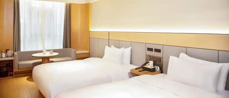 A hotel room with two beds, a small table, a chair, and a nightstand with a lamp and phone.