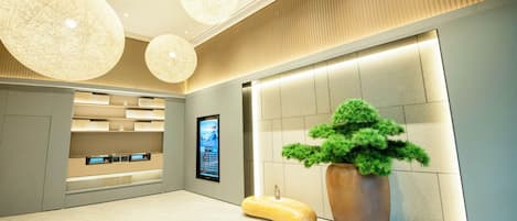 A modern lobby with a reception desk, digital display, and a large potted plant.