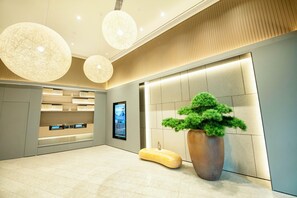 A modern lobby with a large potted plant, a unique seating area, and a digital information screen. - Ji Hotel (Chongqing)