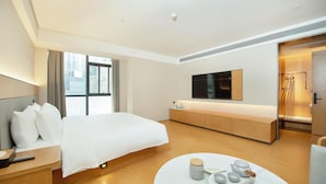 A modern hotel room with a large bed, a bedside table, a round coffee table with tea set, a TV mounted on the wall, and a view of the city through the window. - Ji Hotel (Chongqing)