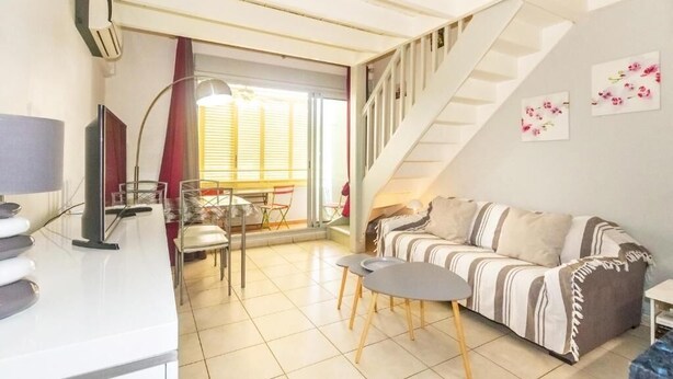 A cozy living room with a striped sofa, a dining area with chairs and a table, and a staircase leading to an upper level. - Purple - Cosy duplex in the heart of L'Hermitage, close to the lagoon (Saint-Paul)