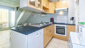 A compact kitchen with wooden cabinets, a dishwasher, an oven, and a coffee maker. - Purple - Cosy duplex in the heart of L'Hermitage, close to the lagoon (Saint-Paul)