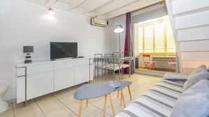 A modern living room with a sofa, a TV, a dining table, and a kitchen area. - Purple - Cosy duplex in the heart of L'Hermitage, close to the lagoon (Saint-Paul)