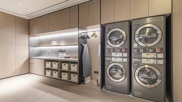 A modern laundry room with four stacked washing machines, a sink, and storage shelves.