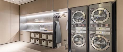 A modern laundry room with four stacked washing machines, a sink, and storage shelves.