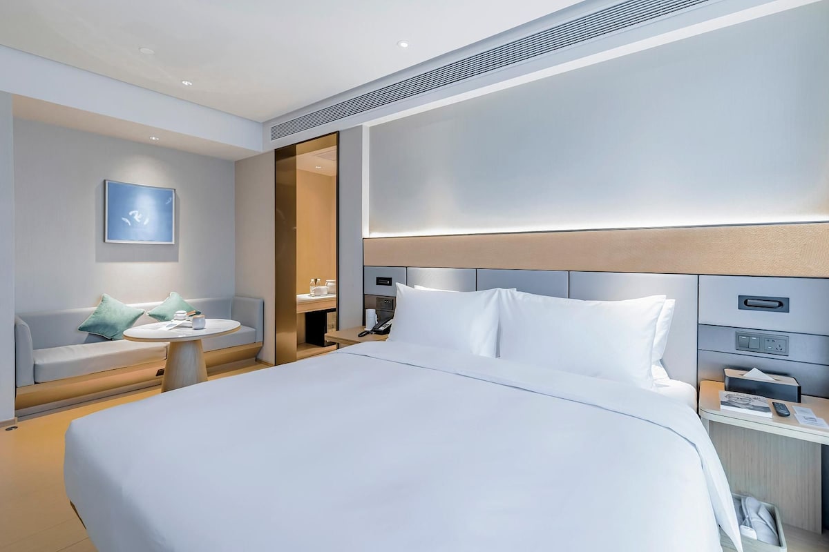 Une chambre d’hôtel moderne dotée d’un grand lit, d’une table de chevet, d’un coin salon avec une petite table et d’un téléviseur fixé au mur.