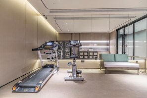 Une salle de sport moderne équipée d’un tapis de course, d’un vélo elliptique et d’un vélo d’appartement, d’un coin salon avec un canapé et d’une grande fenêtre offrant une vue panoramique.