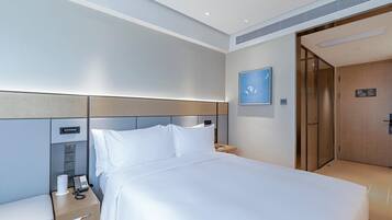 A hotel room with a bed, bedside tables, a phone, and a wall-mounted control panel.