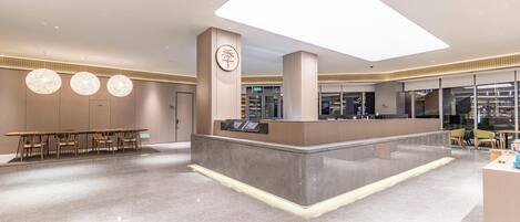 A modern reception area with a central desk, seating area with tables and chairs, and a large illuminated ceiling feature.