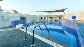 Une piscine sur le toit, avec un décor de mosaïques bleues aux motifs clairs, un parasol et un fauteuil de relaxation bleu.