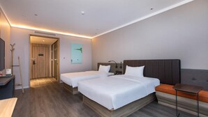 Een hotelkamer met twee bedden, een bureau, een stoel en een deur naar een andere kamer.