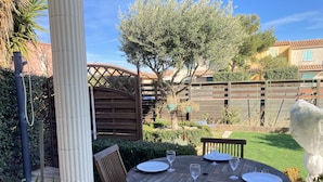 A wooden outdoor dining table set with plates and wine glasses, surrounded by wooden chairs, in a garden with a wooden fence and greenery. - Villa with terrace and garden near the beach (Narbonne plage)