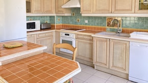 A kitchen with wooden cabinets, a microwave, a toaster, a stove, and a sink. - Villa with terrace and garden near the beach (Narbonne plage)