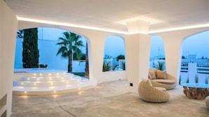 Un interior moderno con una escalera circular, asientos cómodos y ventanas amplias que ofrecen vistas de palmeras y un horizonte urbano distante.