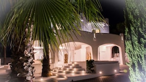 Una casa moderna con fachada clara, una escalera que lleva a un porche cubierto y una palmera en primer plano.