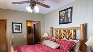 A bedroom with a wooden bed frame, a ceiling fan, a nightstand with a lamp, and a framed picture on the wall. - Making Memories in Red River (Red River)