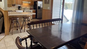 A kitchen with wooden cabinets, a central island, bar stools, a dining table, and a large window with curtains. - Making Memories in Red River (Red River)