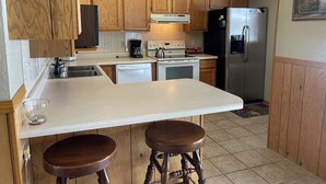 A kitchen with wooden cabinets, a white countertop, a stainless steel refrigerator, a stove, and two wooden stools. - Making Memories in Red River (Red River)