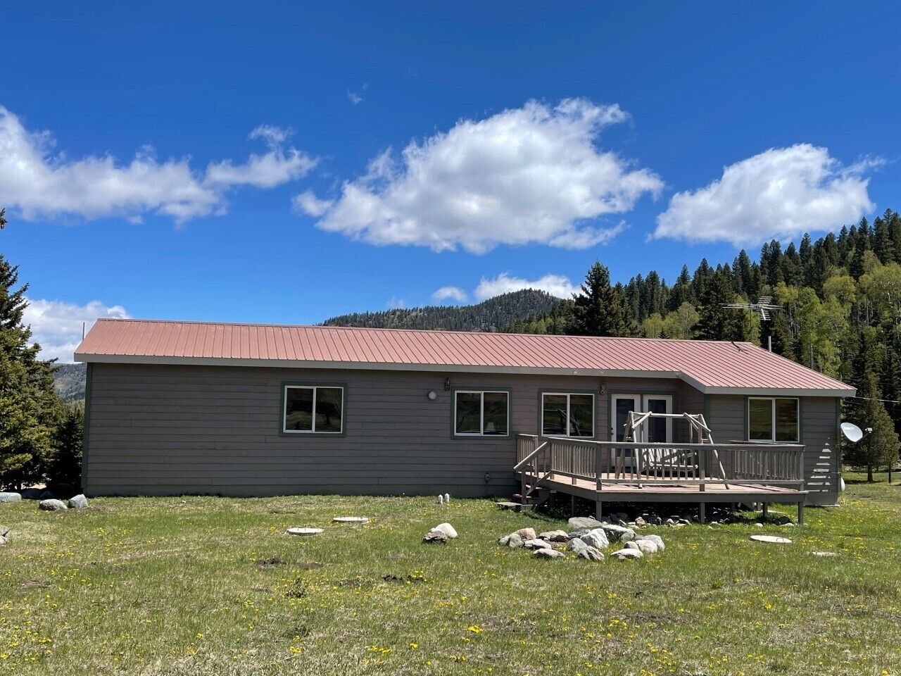 Eine eingeschossige Holzhütte mit rotem Dach, einer Terrasse und einer kleinen Veranda.