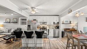 A modern kitchen with white cabinets, stainless steel appliances, and a dining area with black chairs and a wooden table. - DL403 Tranquility Shore by First Flight Rentals (Nags Head)