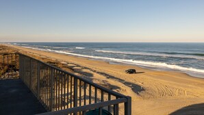 A beach with a wooden walkway and a vehicle parked on the sand. - DL403 Tranquility Shore by First Flight Rentals (Nags Head)