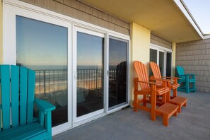 A balcony with sliding glass doors, outdoor seating, and a view of the ocean.