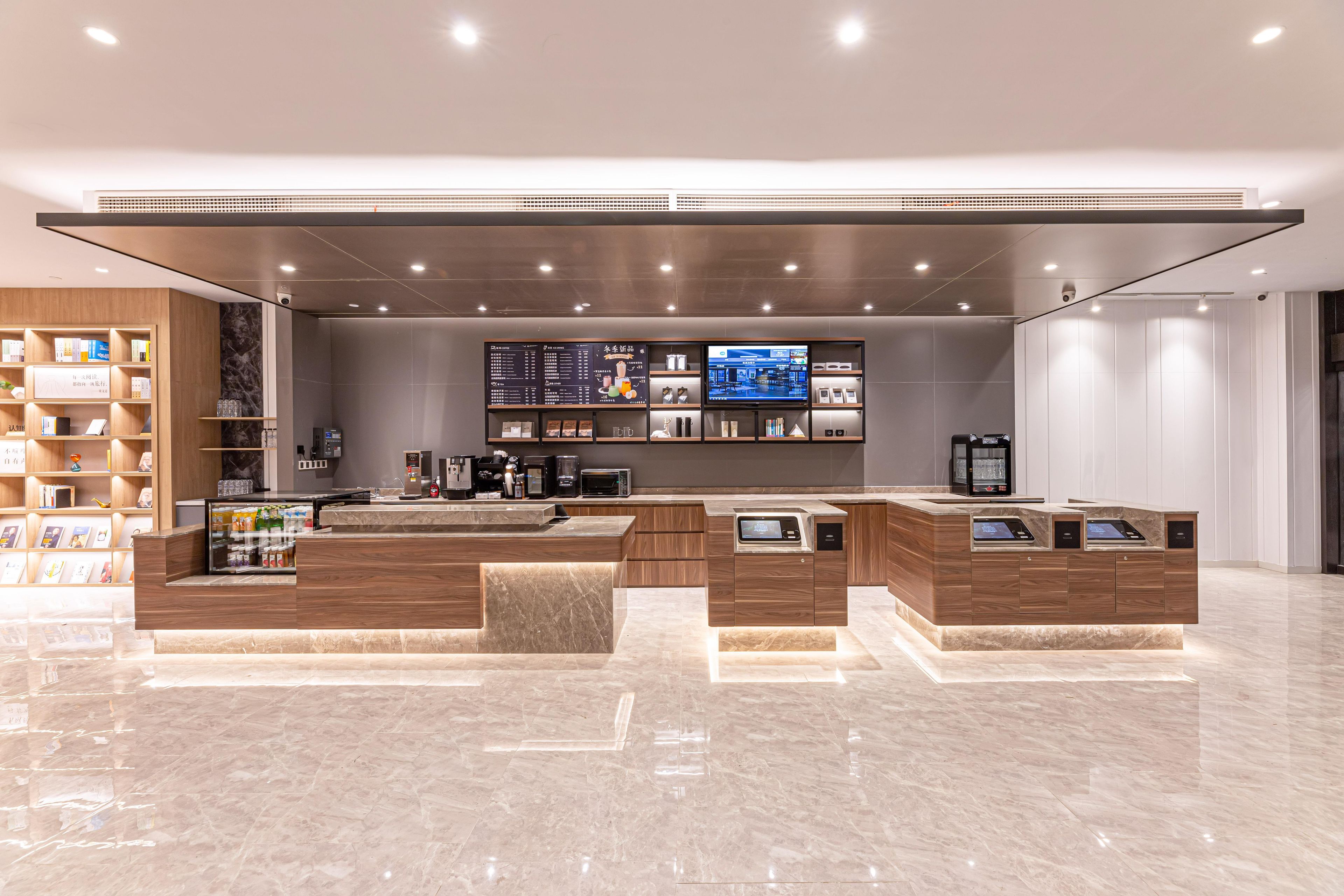 A modern reception area with a marble floor, wooden reception desk, digital information screens, and a bookshelf with magazines.