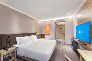 Et moderne hotelværelse med en stor seng, et skrivebord, et fjernsyn og et badeværelse, der kan ses gennem en åben dør.