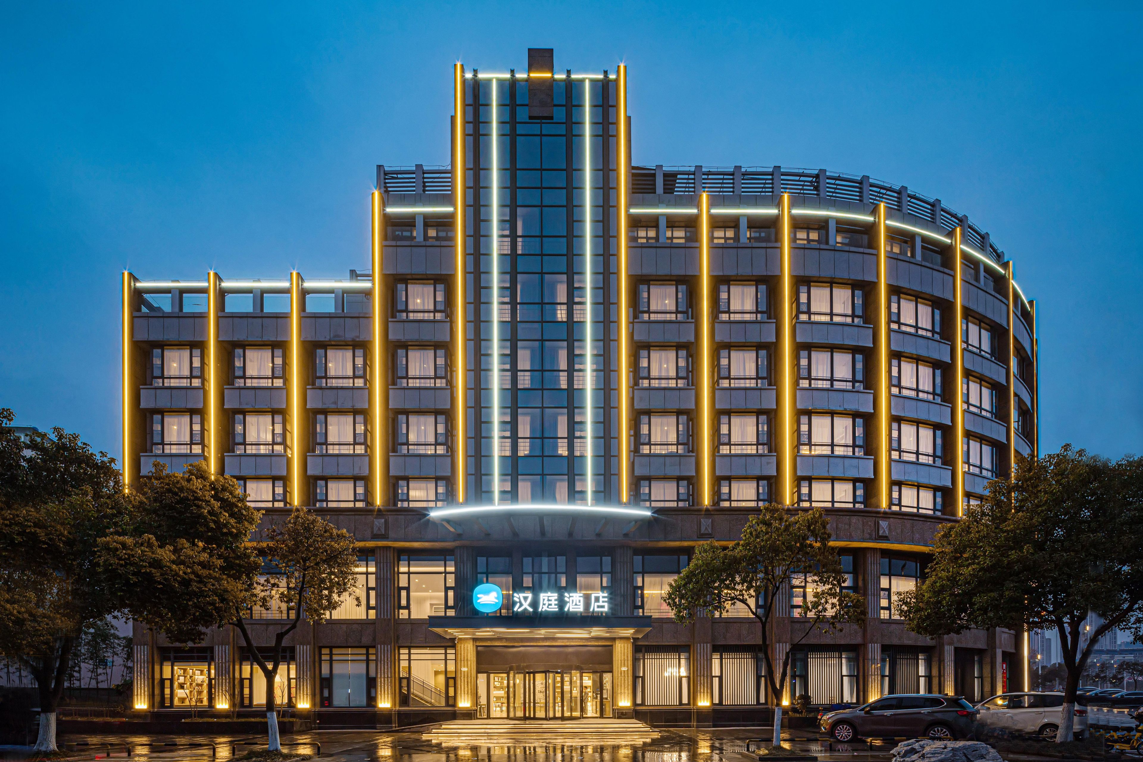 Un hôtel moderne doté d’une bande lumineuse verticale bien visible, d’une entrée centrale et d’une conception architecturale circulaire.