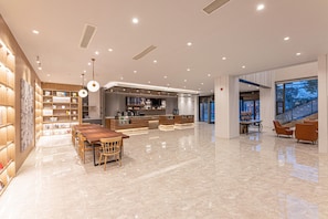 A spacious lobby with a wooden reception desk, a dining area with a long table and chairs, and a modern staircase.