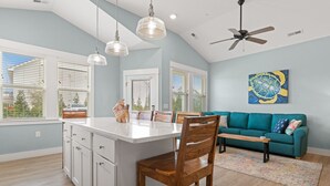 Une cuisine moderne avec un îlot central, des chaises en bois, un canapé de couleur turquoise et un ventilateur de plafond.