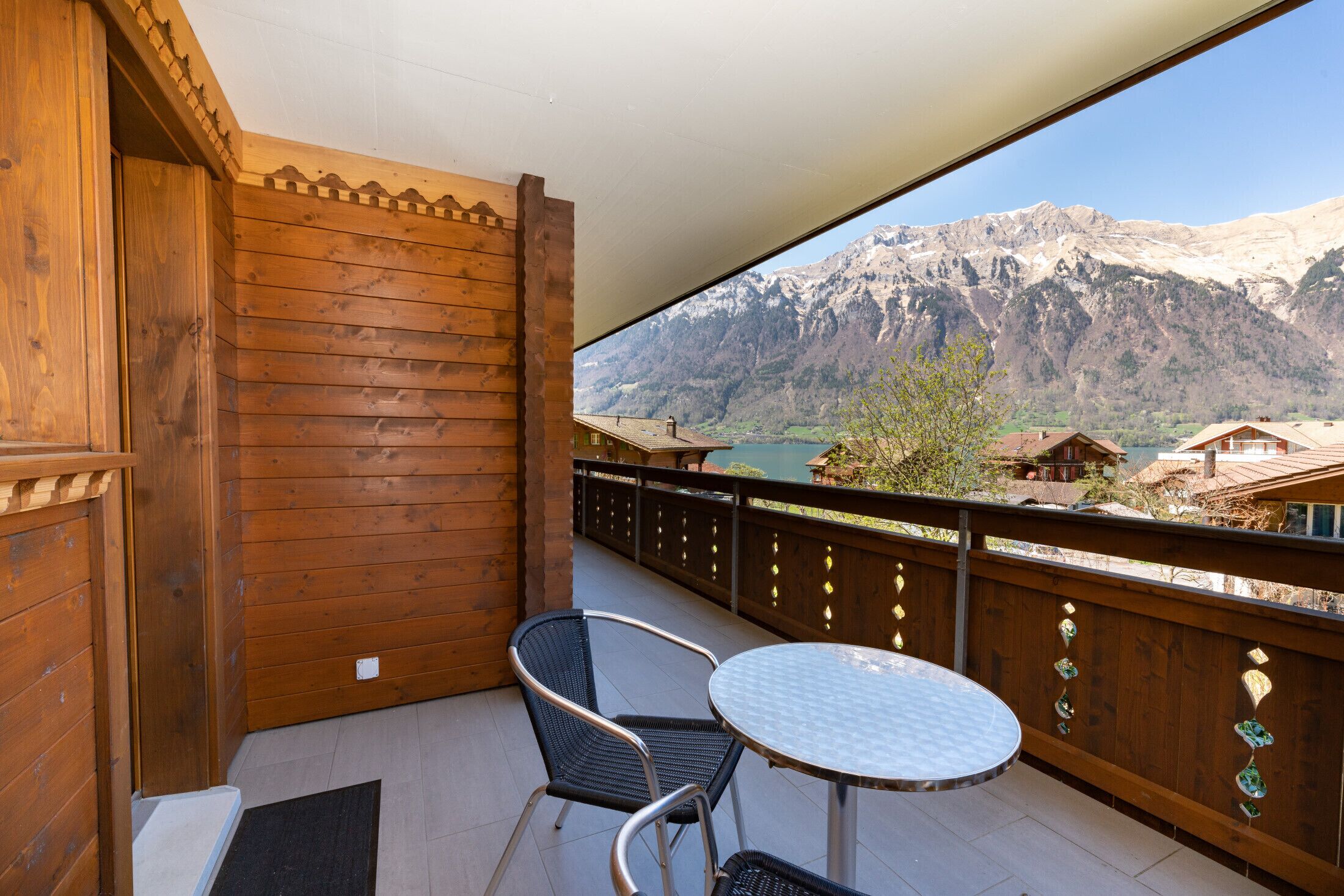 A wooden balcony with a table and chairs, overlooking a mountainous landscape.