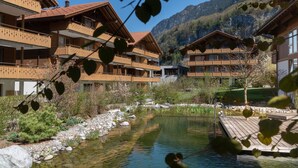 A hotel with multiple wooden balconies overlooking a mountain landscape and a small pond. - Chalet Apartments Iseltwald (Iseltwald)