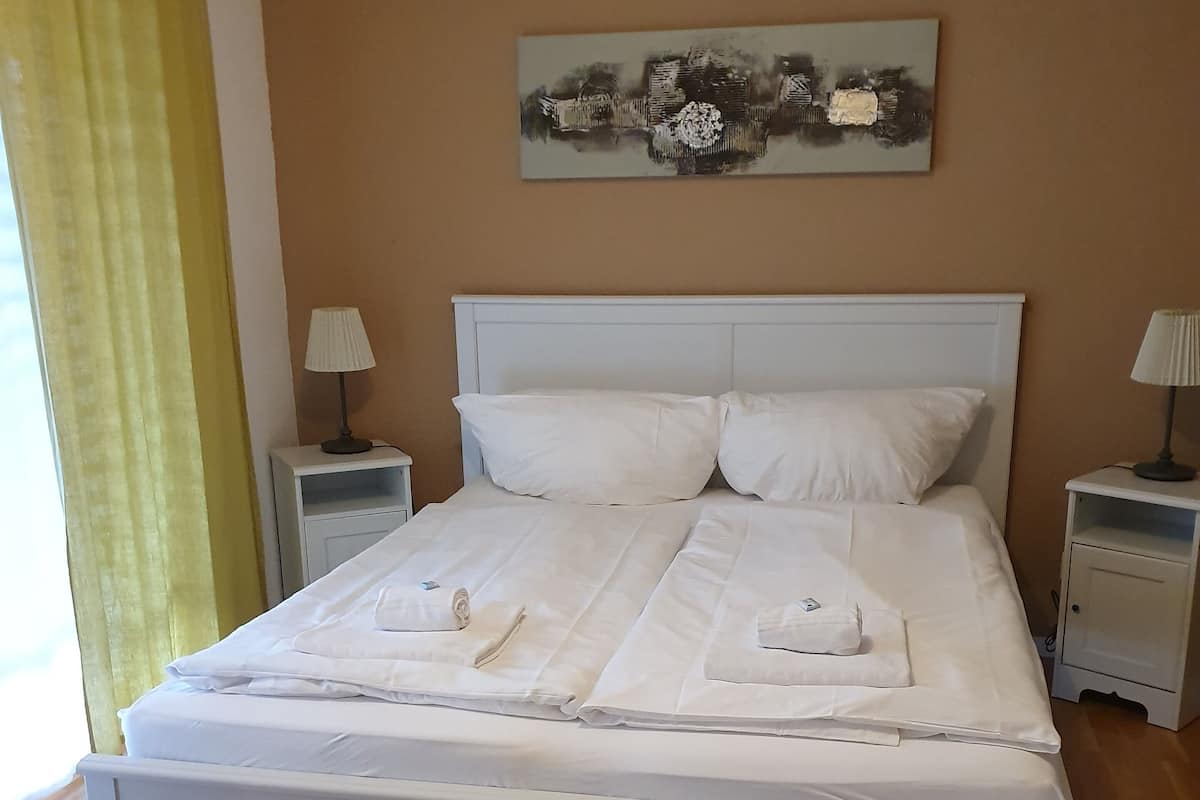 A neatly made bed with white linens and pillows, two bedside tables with lamps, and a painting on the wall.