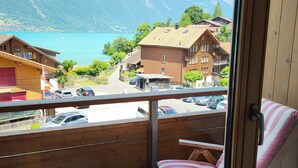 A balcony with a wooden floor, a striped cushion, and a view of a lake and mountains. - Chalet Apartments Iseltwald (Iseltwald)